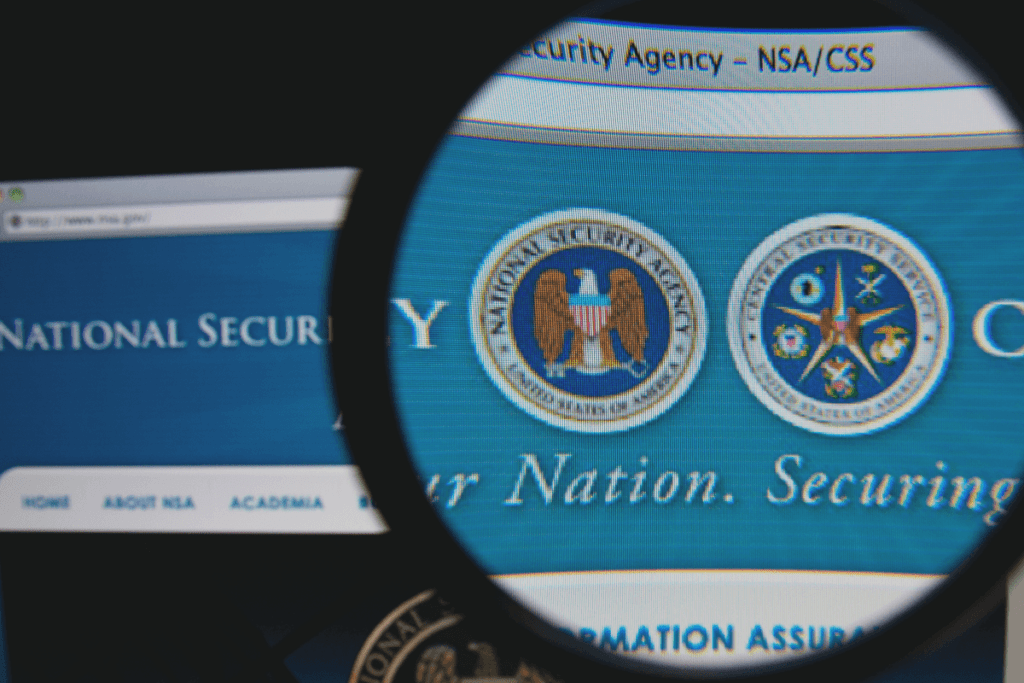 A magnifying glass is held before the NSA logo