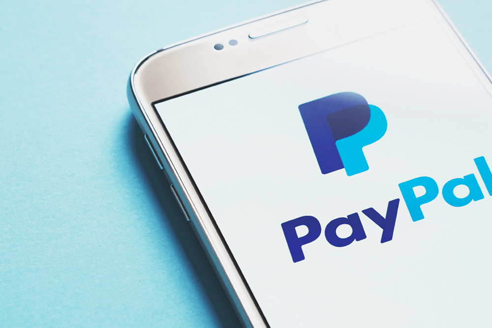 A white phone rests on a blue background while displaying the PayPal logo