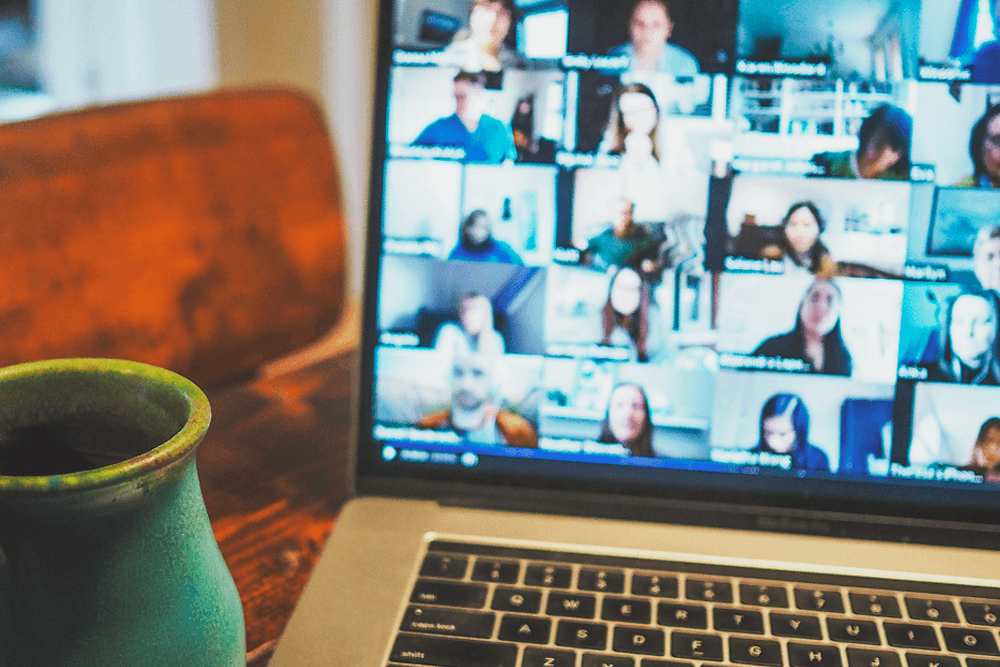 A laptop shows a group of people chatting over video-conference