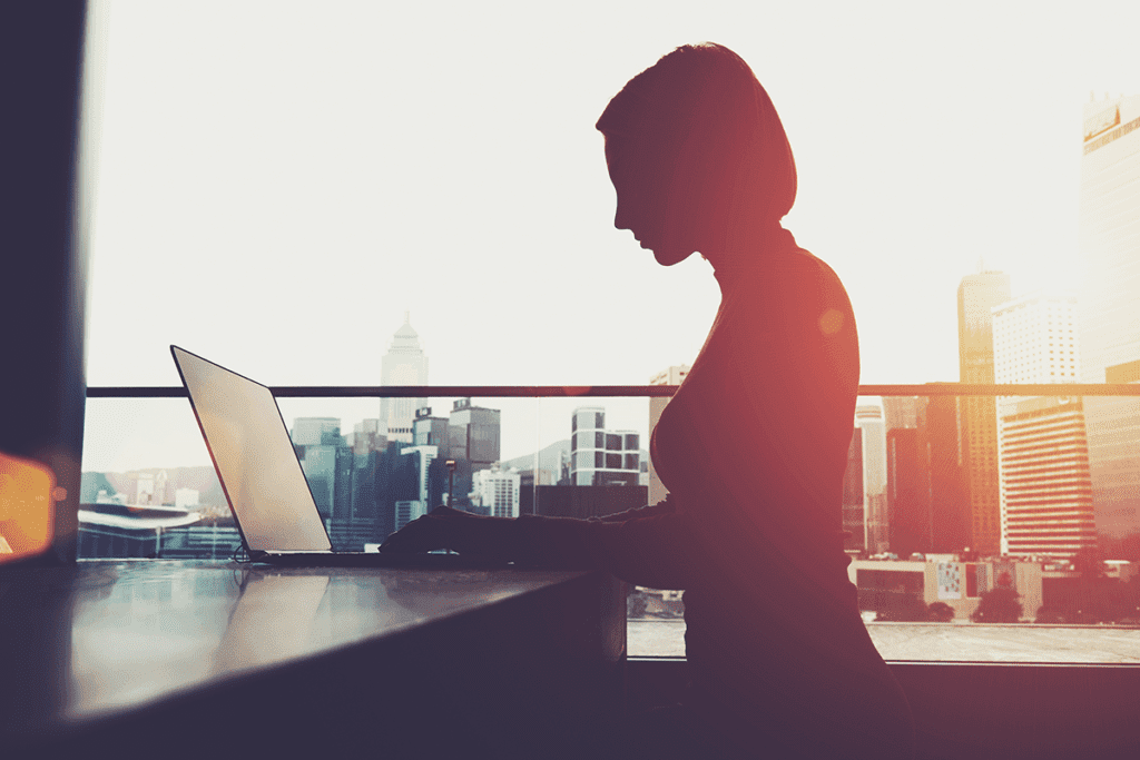 A silhouette of a woman's profile view on a laptop against a city skyline