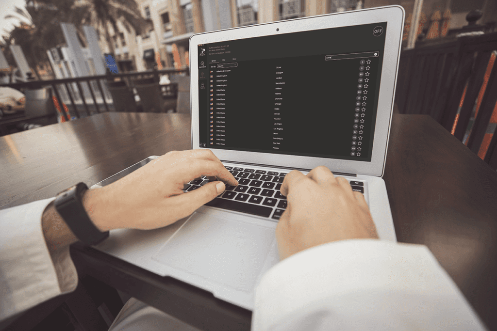 A person on their laptop at an outdoor care types to find a server in theSilverBackVPNlocation list. Why use vpn? For safety.
