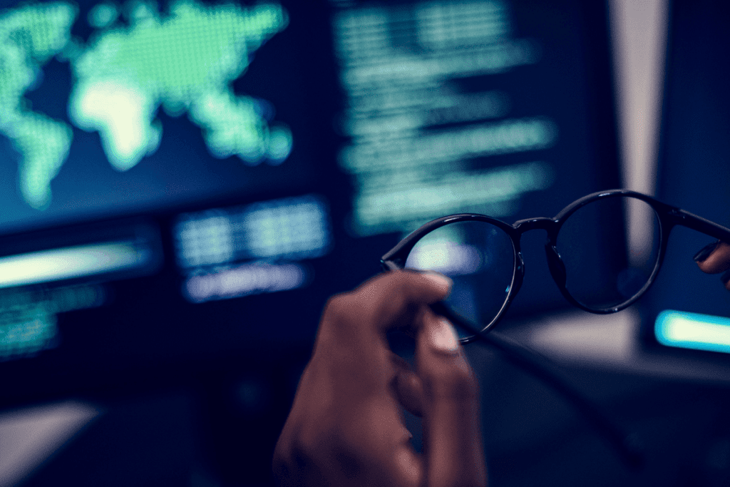A person holds black framed glasses while reviewing their computer screen of code and network upgrade data