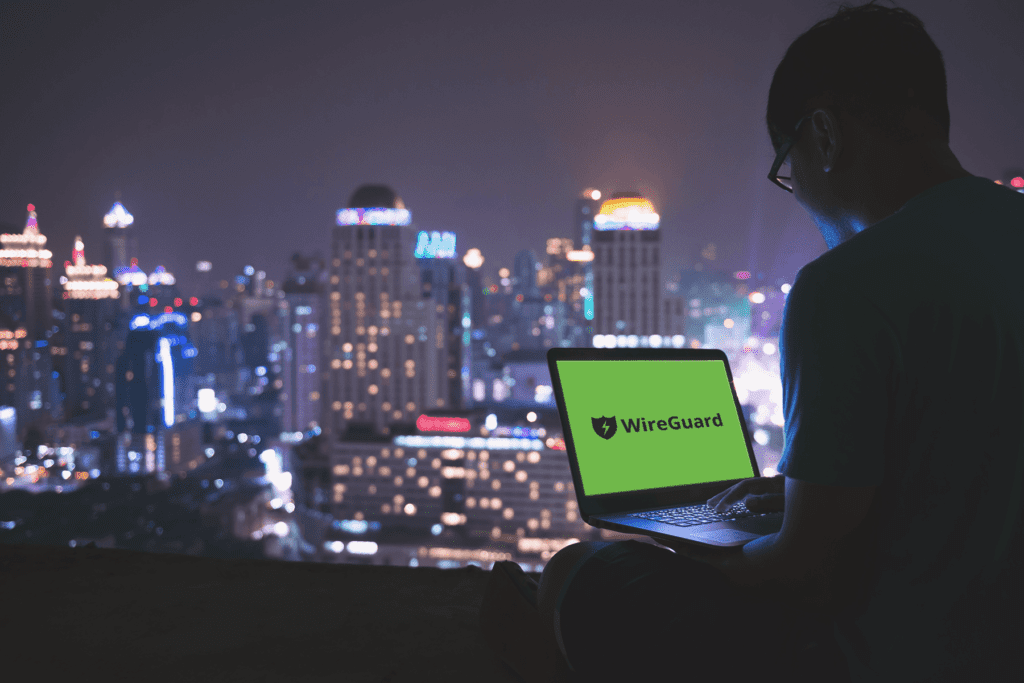Man sits outside overlooking city while on laptop, WireGuard VPN text is displayed on green background