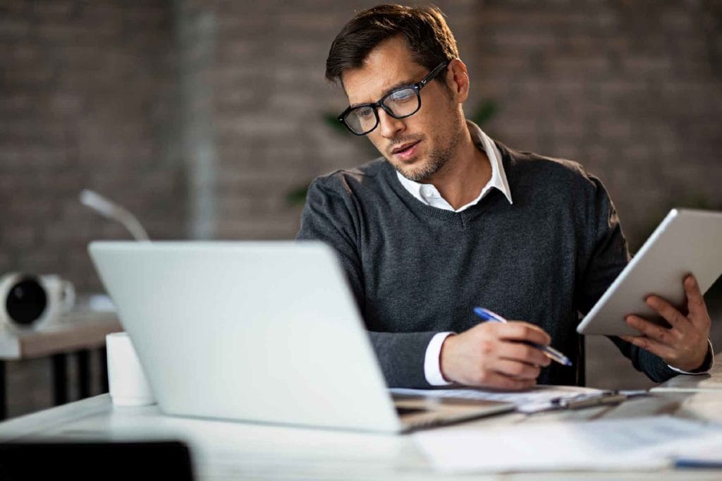 Man working on laptop and holding a tablet