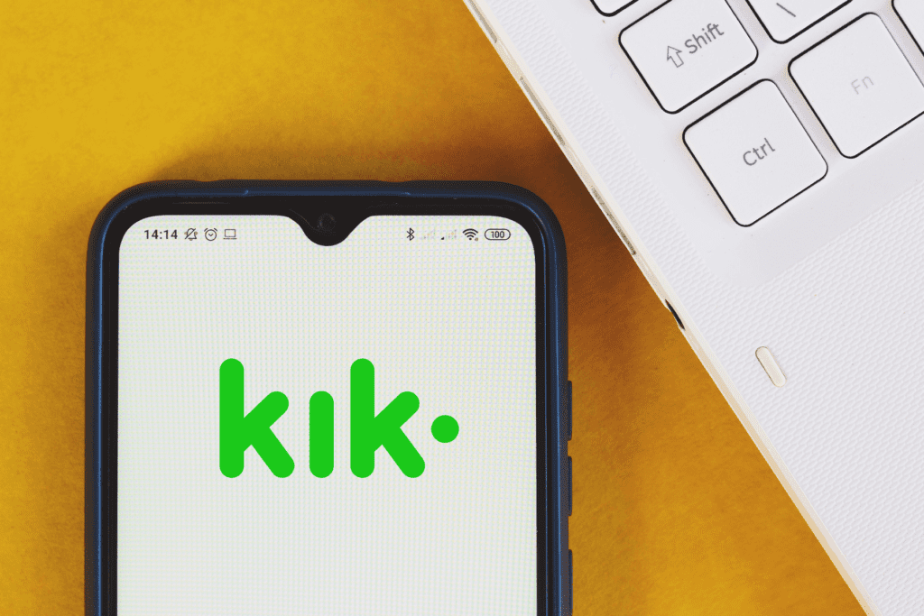 A phone displays the logo for Kik on its screen beside a laptop keyboard to visualize how to delete kik