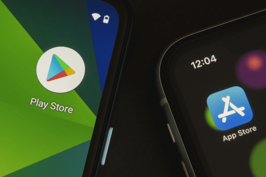 Two phones sit on a table side by side, with the phone on the left displaying the Google app store and the phone on the right displaying the Apple App Store. Visualizing how to change app store country.