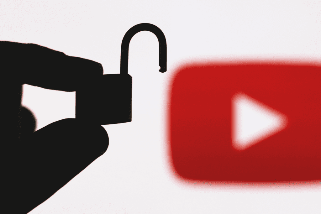 A silhouetted hand holds an unlocked padlock in front of a blurry background to visualize an unblocked YouTube