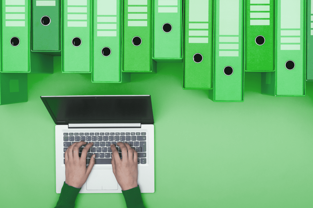 A laptop is used beside binders, visualizing digital organization