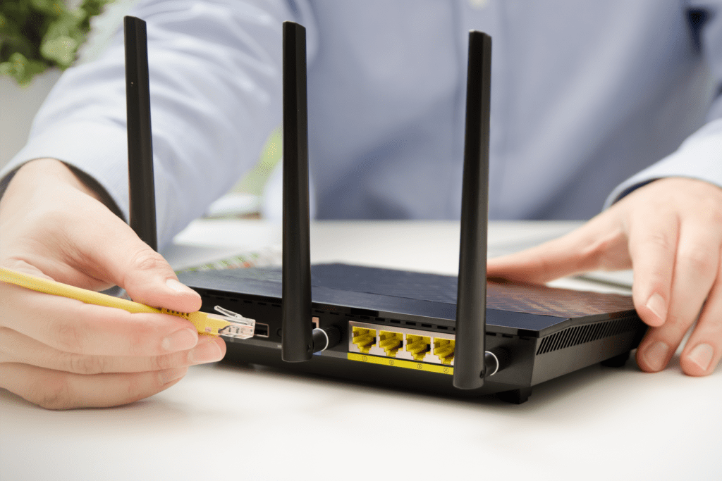 A person plugs a yellow ethernet cable into the back of their WiFi router, visualizing the differences of ethernet vs WiFi
