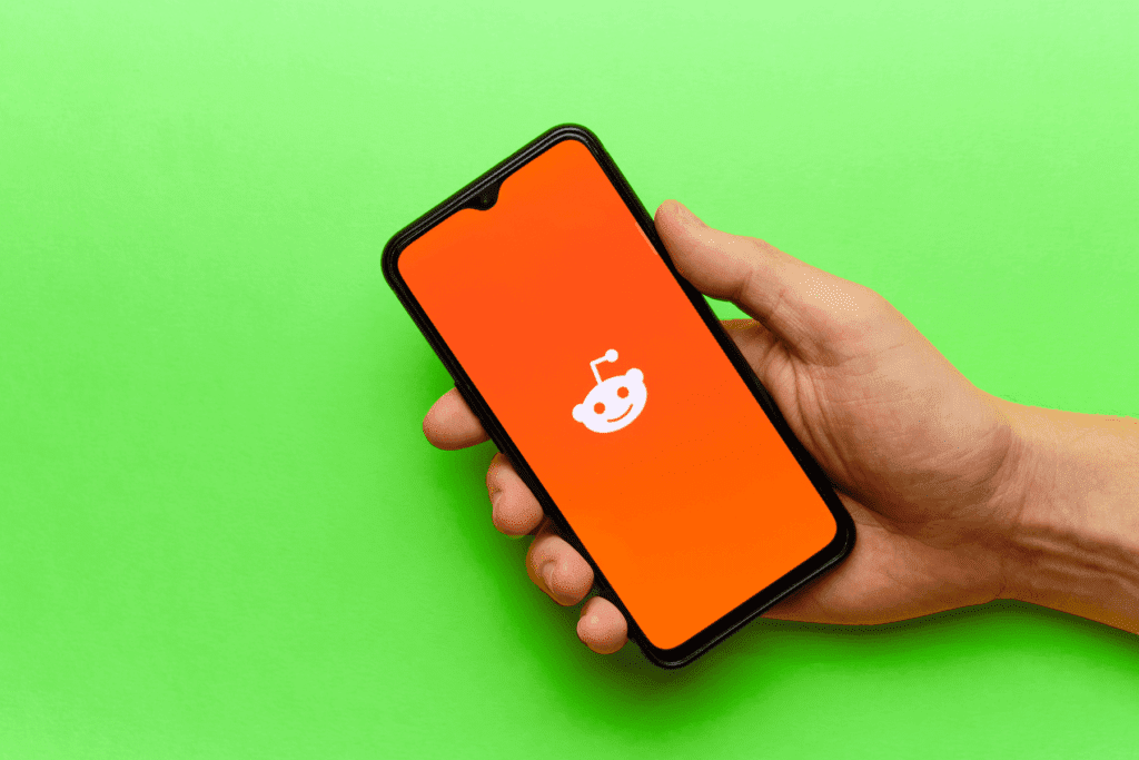 A person holds their smartphone open to the Reddit app as they wonder to to delete Reddit account details from their device.