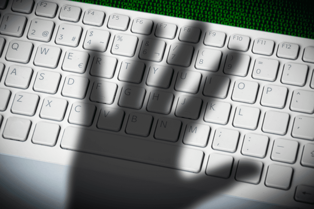 The shadow of a hand is cast over a keyboard to imply spying or dubious activity such as bossware