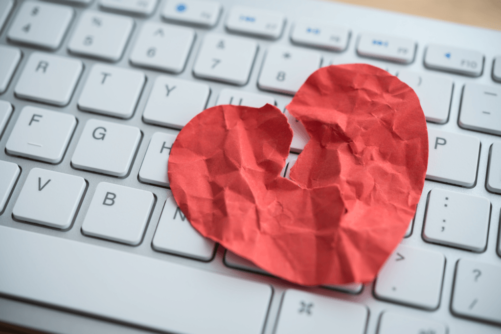 An image of a keyboard with a crinkled and ripped paper heart on it to visualize the emotional damage potentially caused by romance scams.