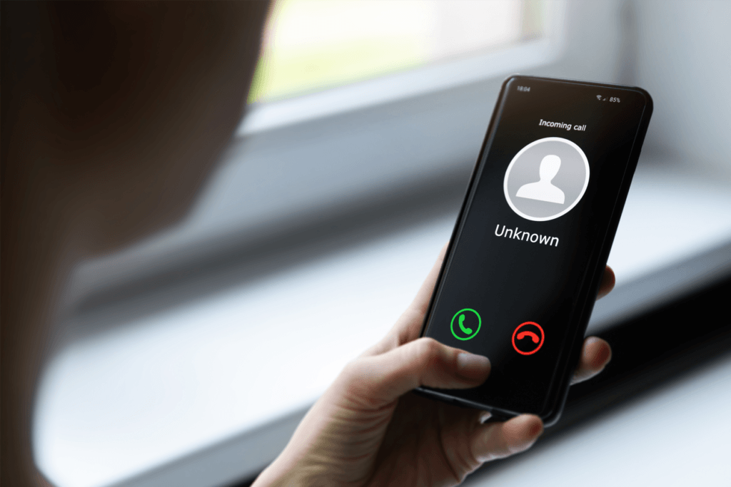 A person is seen using their phone with the display indicating an unknown caller is on the other end of the line