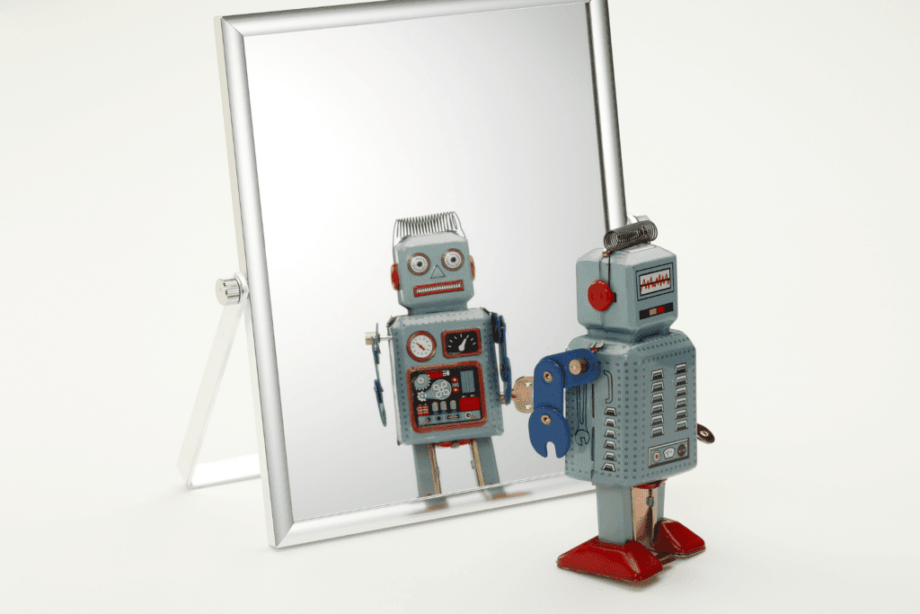 Photo of a toy robot looking in the mirror to symbolize an AI mirror test.
