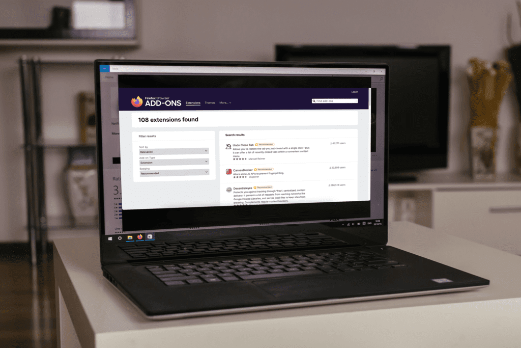 A laptop sits on a white table with the display open to the Firefox Add-ons page which is where most Firefox VPN extensions are installed from