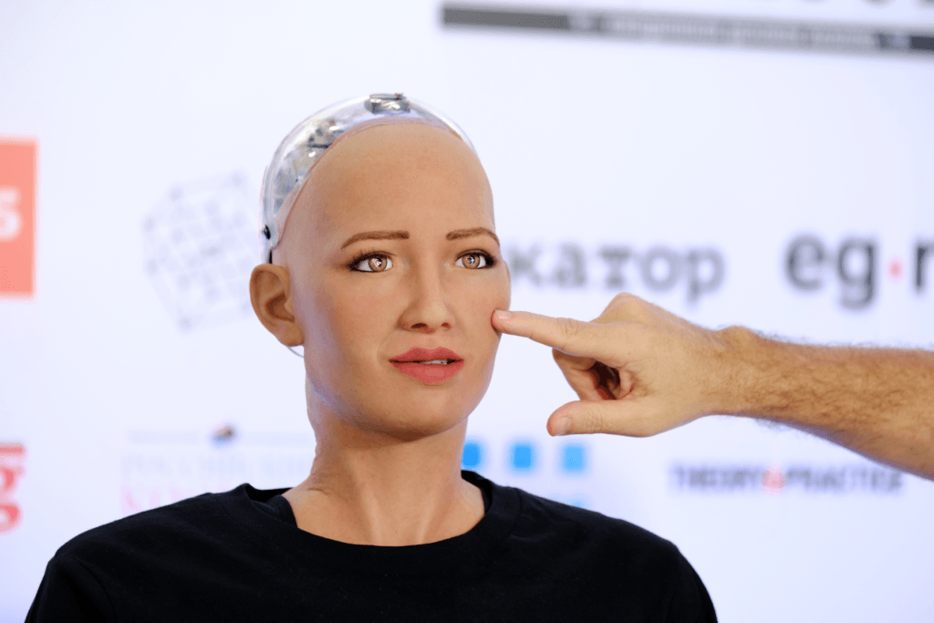 An image of Sophia the robot being poked by a human to symbolize our curiosity for robots.