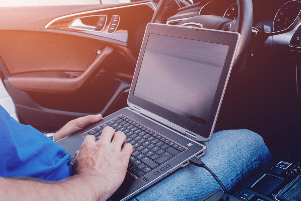 A man uses a laptop from the driver's seat of a vehicle, demonstrating what wardriving looks like