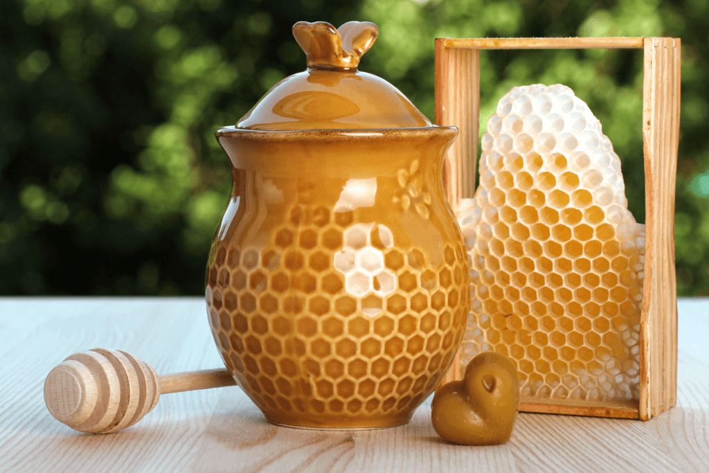 a picture shows a honeypot jar resting beside a honey wand and some honeycomb