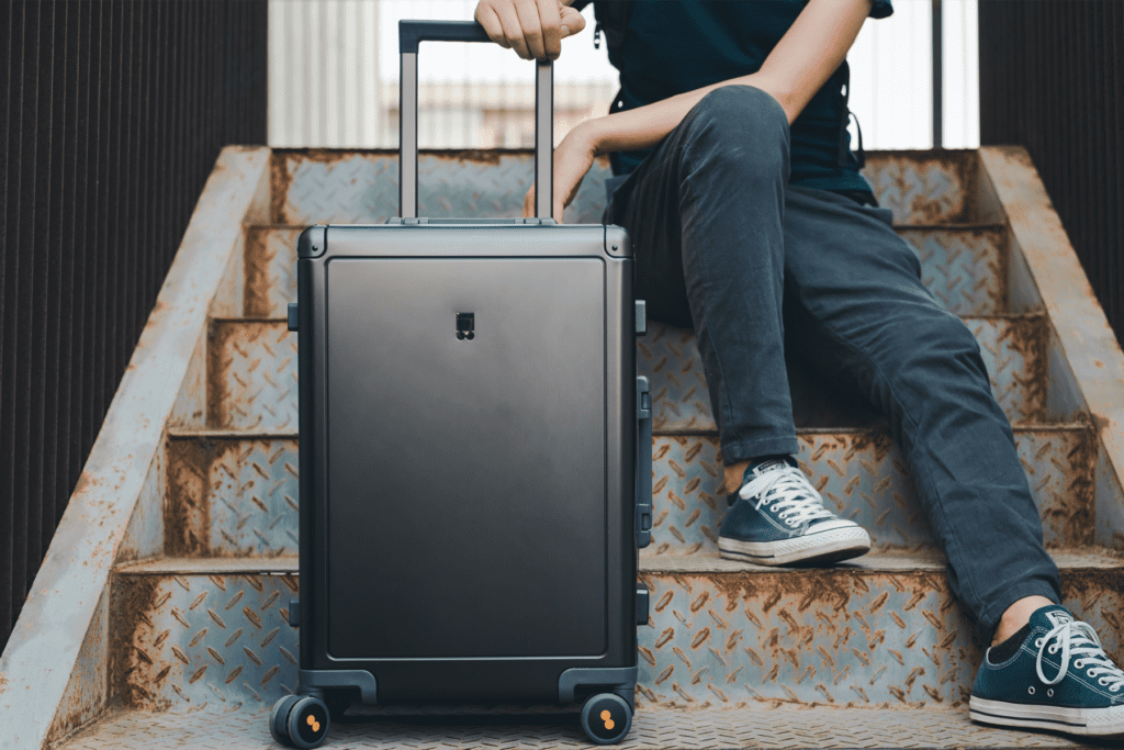 A person sits on steps with black rectangular rolling suitcase to accompany luggage tracker tips