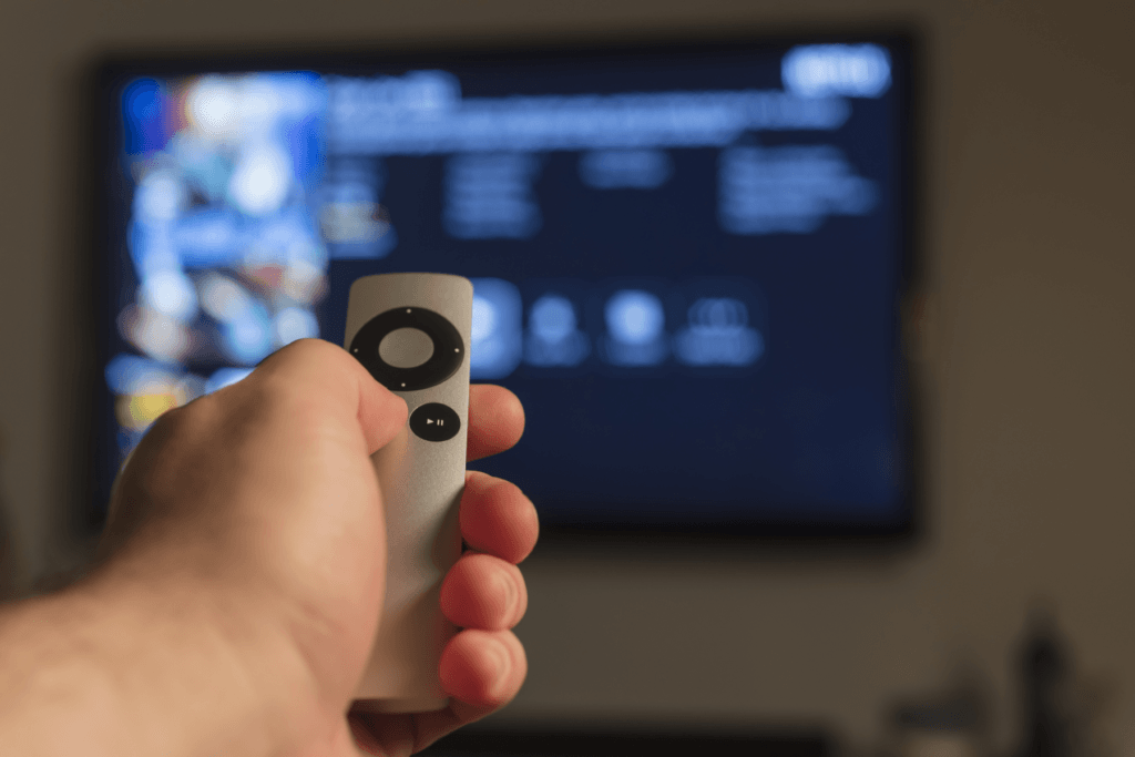 Photograph of a person's hand holding a remote up to their TV to simulate accessing a VPN for Apple TV.