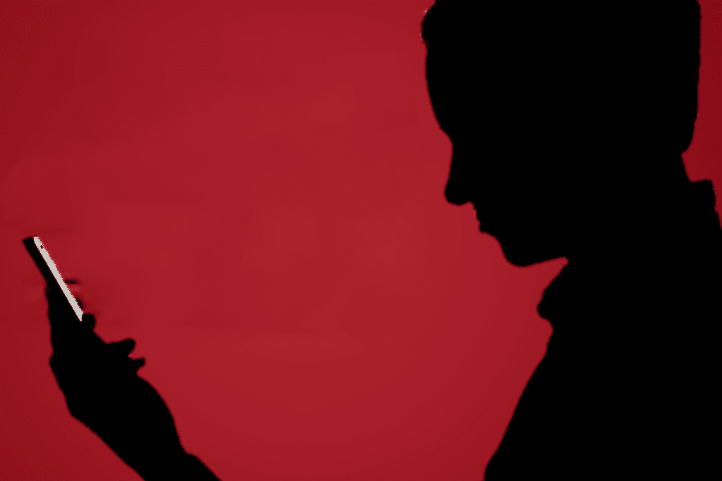 A silhouette of a person against a red background looking at their phone to depict zero-click attacks