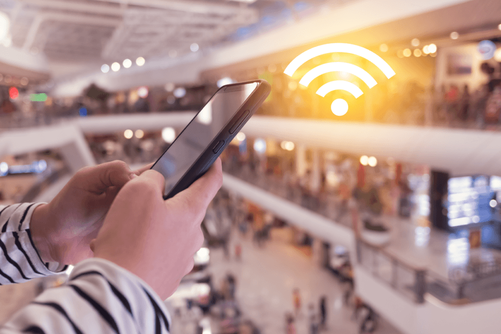 A person uses their phone in a public shopping area visualized with Wi-Fi symbol to answer the question does a VPN work without Wi-Fi?