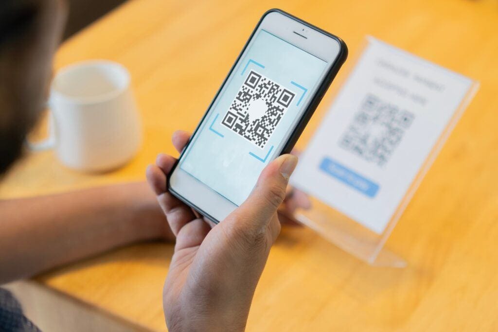 Selective focus of man's hand scanning QR code through mobile phone, what is quishing
