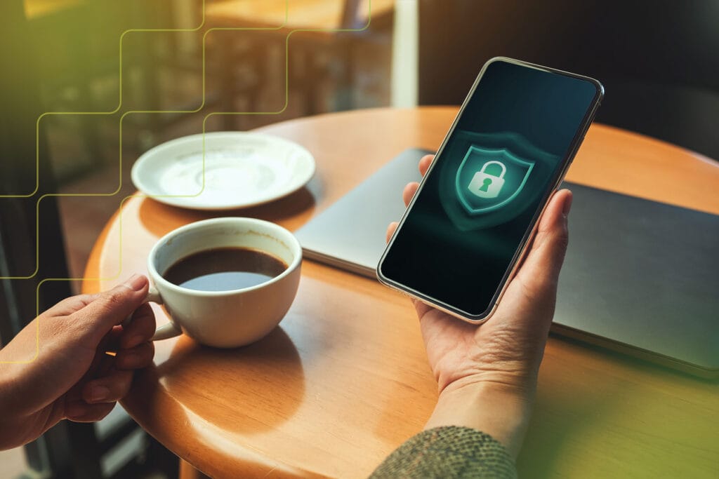 A mobile phone user in a cafe looking at a phone screen displaying a green padlock which conveys VPN App Security: How to Spot a Vulnerable VPN Client